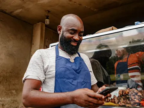 A food seller in an apron checking his phone at his counter