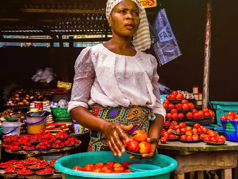 A woman picking tomatoes from a bucket at her market stall